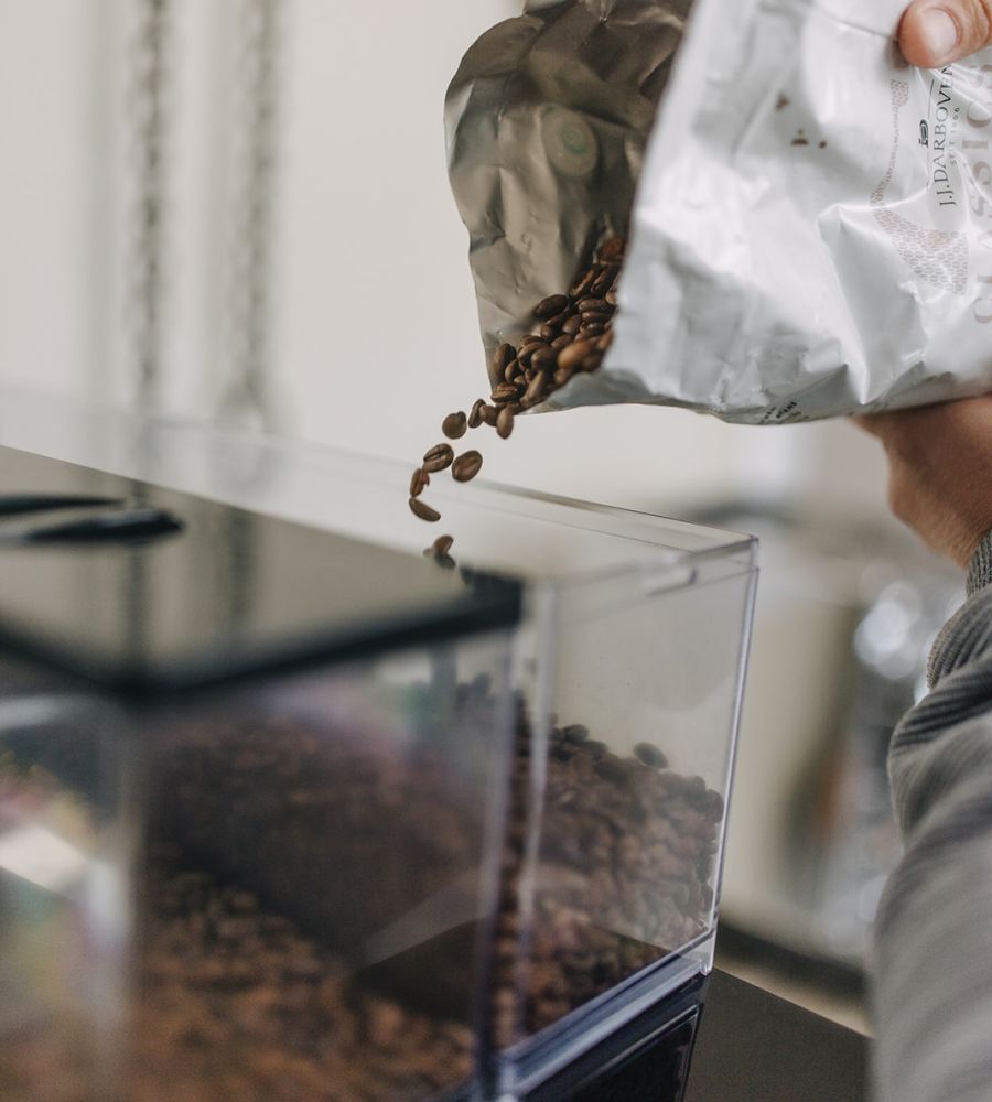 Kaffeebohnen werden aus einer geöffneten Tüte in den Bohnenbehälter einer Kaffeemaschine gefüllt.