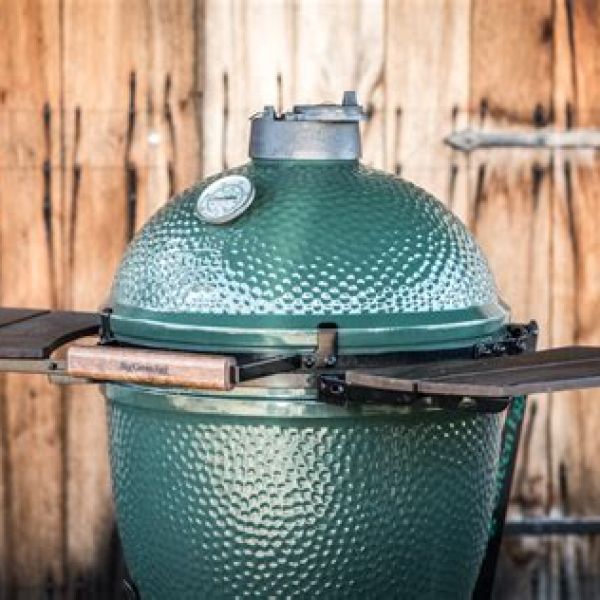 Grüner Big Green Egg Keramikgrill in großer Ausführung mit aufgeklappten Seitentischen vor Holzwand.