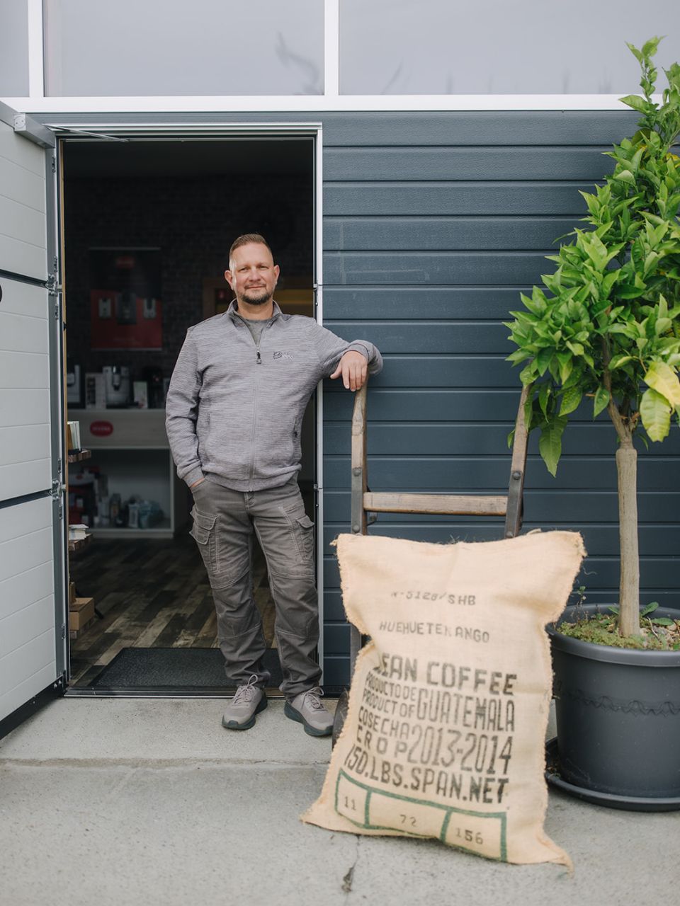 Inhaber von Bahro Kaffeemaschinen steht vor dem Laden neben Kaffeesack und Pflanze.
