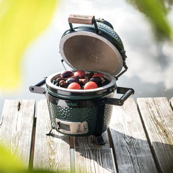Kleiner grüner Keramikgrill Big Green Egg Mini auf einem Holzsteg am Wasser, gefüllt mit frischem Obst.