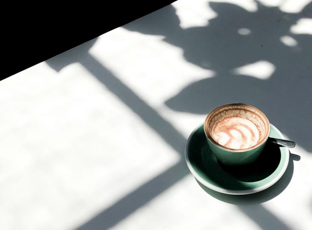 Cappuccino in türkiser Tasse auf weißem Tisch im Sonnenlicht mit weichen Schatten.