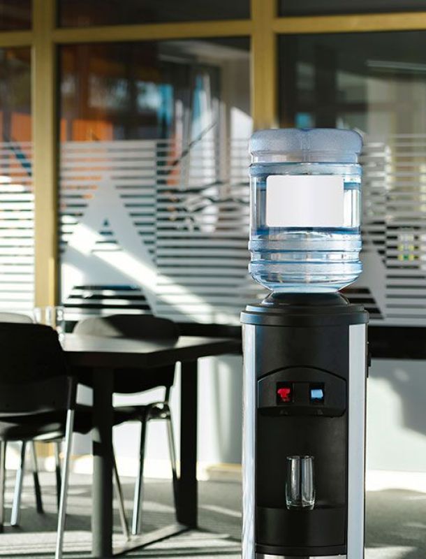 Wasserspender mit aufgesetzter Wasserflasche in einem modernen Konferenzraum mit Stühlen und Glastür.