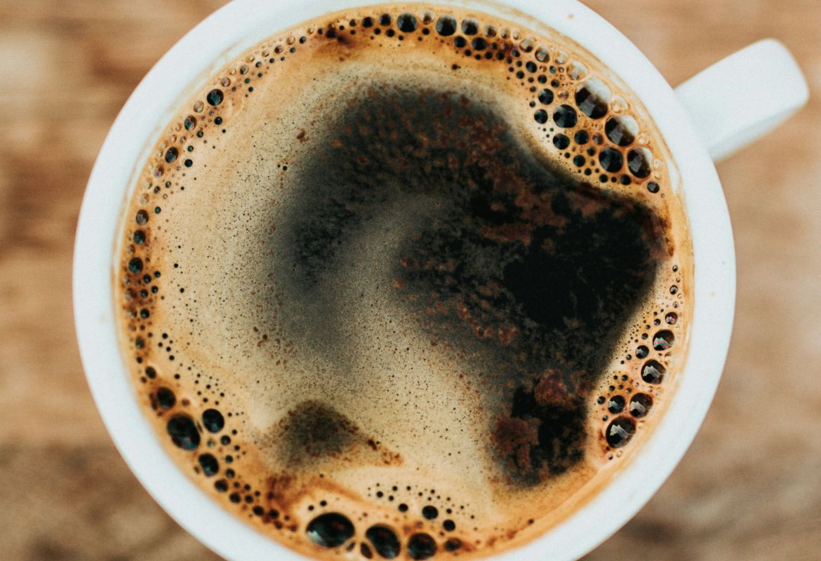 Kaffee in einer weißen Tasse aus der Vogelperspektive, mit dunkler Crema und Blasen auf rustikalem Holztisch.