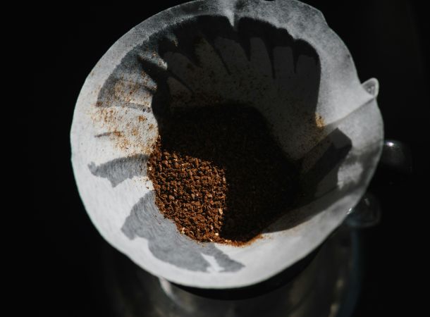Kaffeefilter mit frisch gemahlenem Kaffeepulver in einer Pour-Over-Kanne im Schattenlicht.