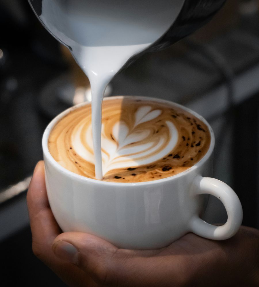 Barista gießt cremigen Milchschaum in eine Tasse Cappuccino mit Latte-Art.