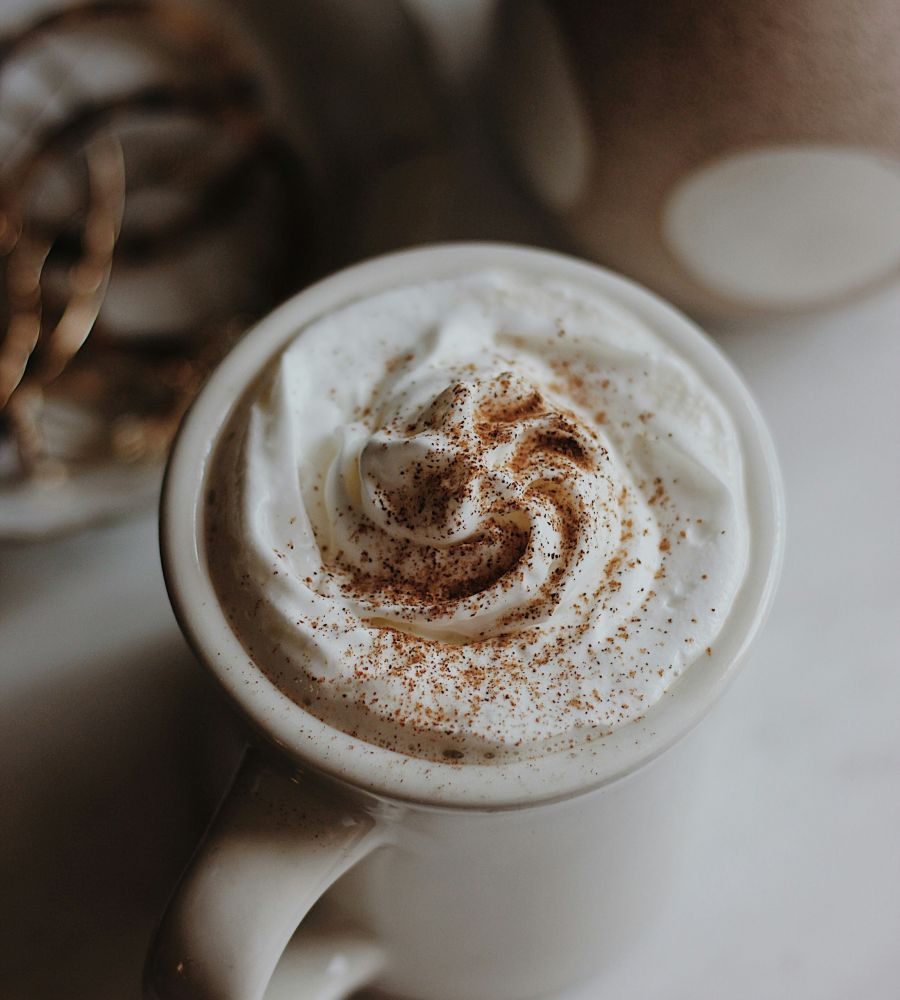 Tasse Kaffee mit einer großzügigen Haube aus Schlagsahne und Zimt auf weißem Tisch.