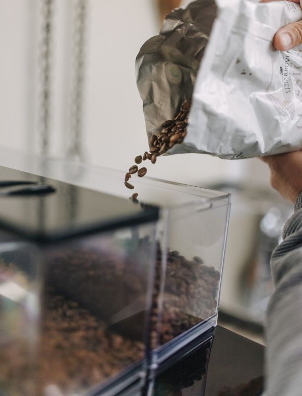 Kaffeebohnen werden aus einer geöffneten Tüte in den Bohnenbehälter einer Kaffeemaschine gefüllt.