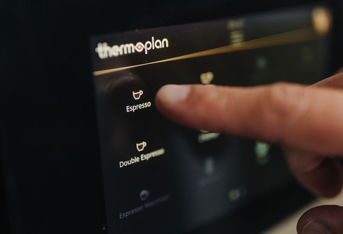 Finger wählt über das Thermoplan-Touchdisplay einen Espresso auf der Kaffeemaschine aus.