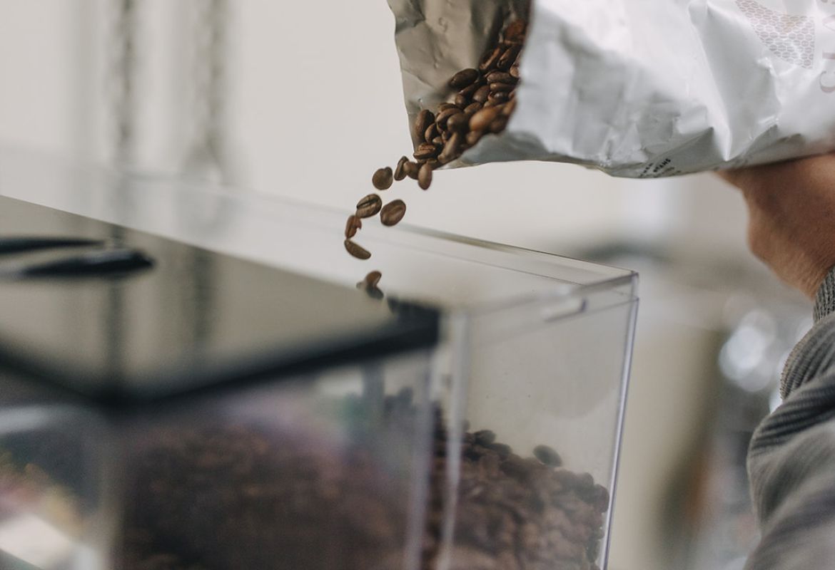 Kaffeebohnen werden aus einer geöffneten Tüte in den Bohnenbehälter einer Kaffeemaschine gefüllt.