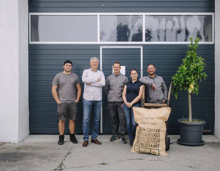 Team von Bahro Kaffeemaschinen vor dem Firmengebäude mit Kaffeesack und Pflanze.