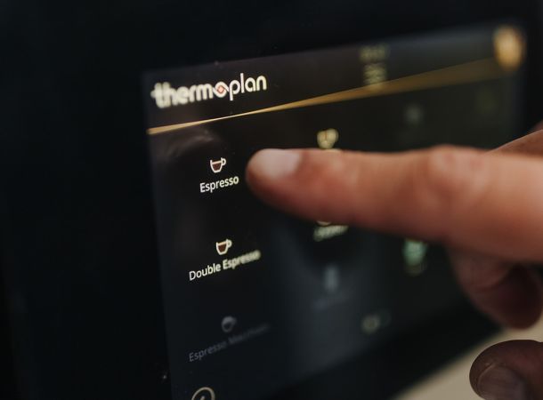 Finger wählt über das Thermoplan-Touchdisplay einen Espresso auf der Kaffeemaschine aus.