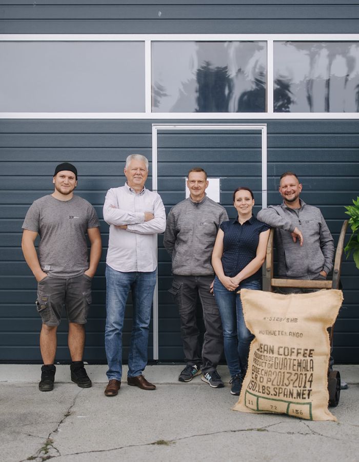 Team von Bahro Kaffeemaschinen vor dem Firmengebäude mit Kaffeesack und Pflanze.