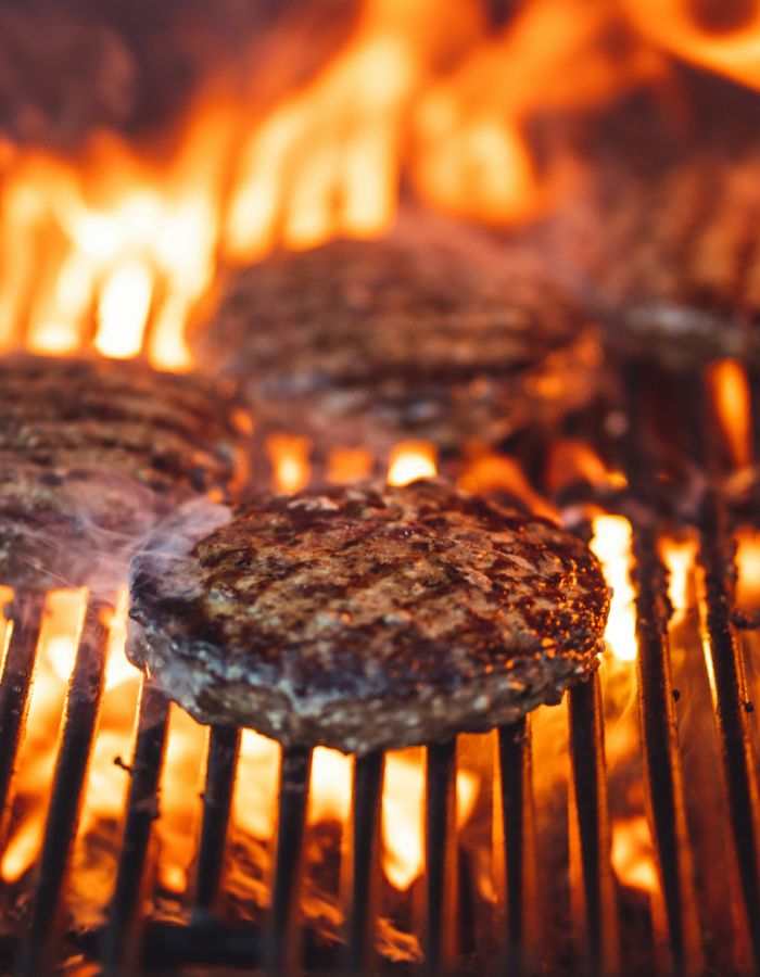 Burger-Patties auf einem heißen Grill mit offenen Flammen und intensiver Hitze.